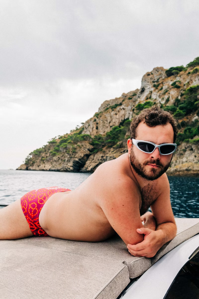 Red mens swim brief with a pretzel pattern  by the water 